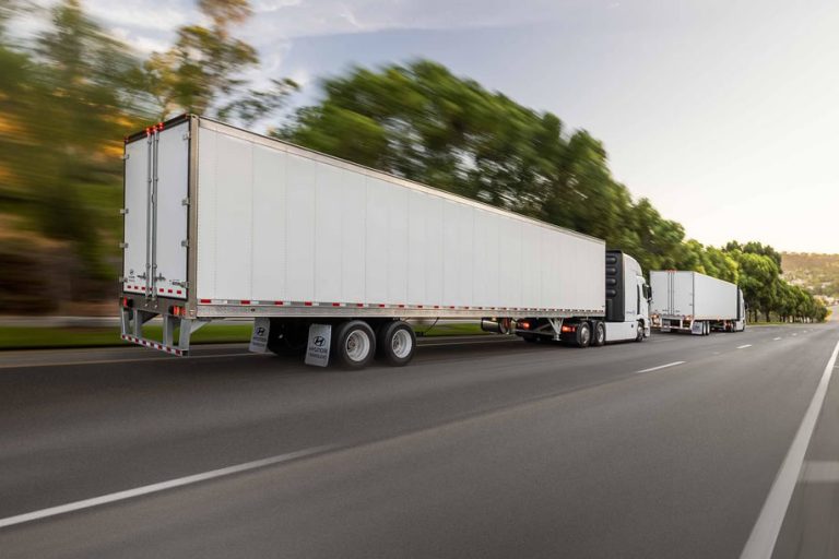 2 white Hyundai Translead trailers driving down a highway.
